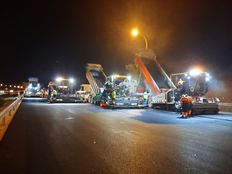 Extendedora y camiones de mezcla bituminosa trabajando de noche en la M-50